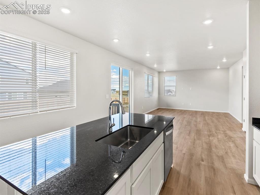 Image 7 of 24: Kitchen with dark stone countertops, white cabinetry, light wood-style floo