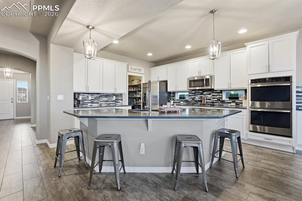 Image 8 of 49: 36 in cabinets, quartz countertops. double ovens, tile backsplash, and larg