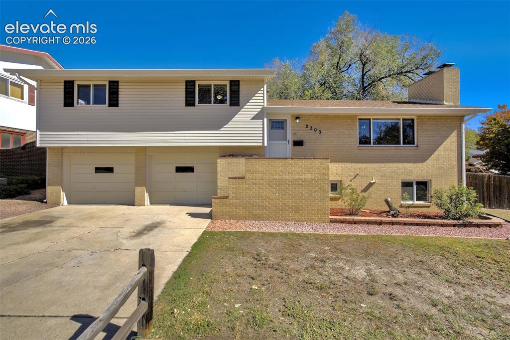 Caption: Split-level exterior featuring tan brick masonry, horizontal vinyl siding, a two-car garage, and a c