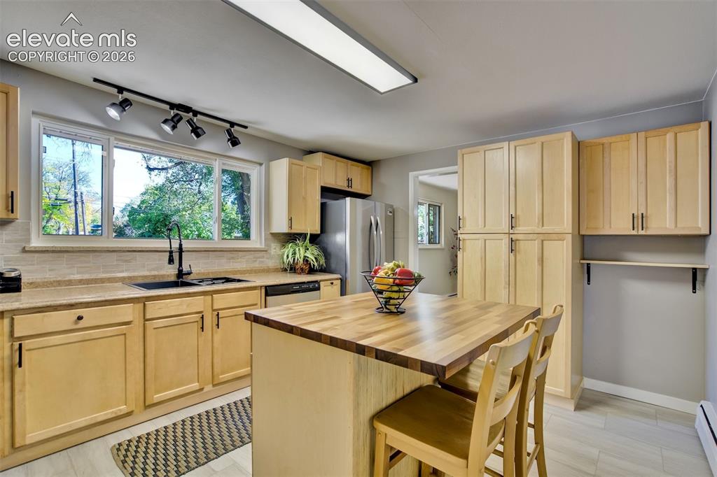 Image 16 of 50: Kitchen featuring light-tone wood cabinetry, central island with a wood cou