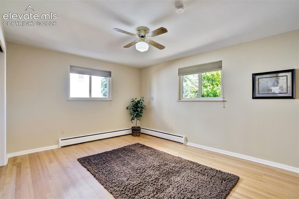 Image 28 of 50: Neutral-toned room featuring wood-finish flooring, dual windows with fitted