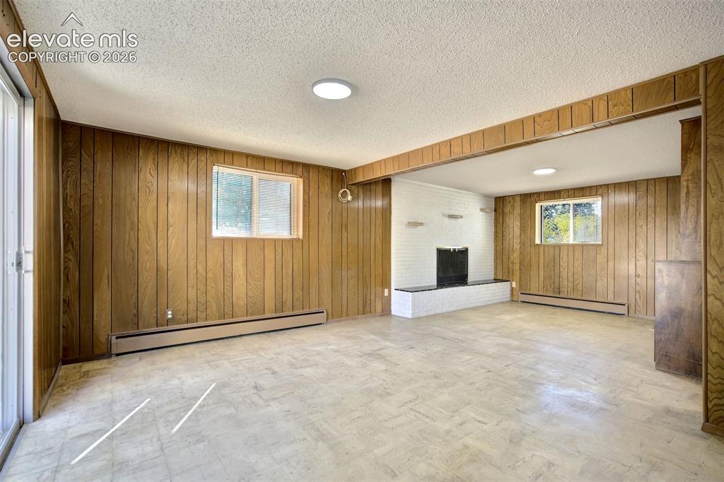 Image 38 of 50: Interior space featuring wood-paneled walls, a white painted brick fireplac