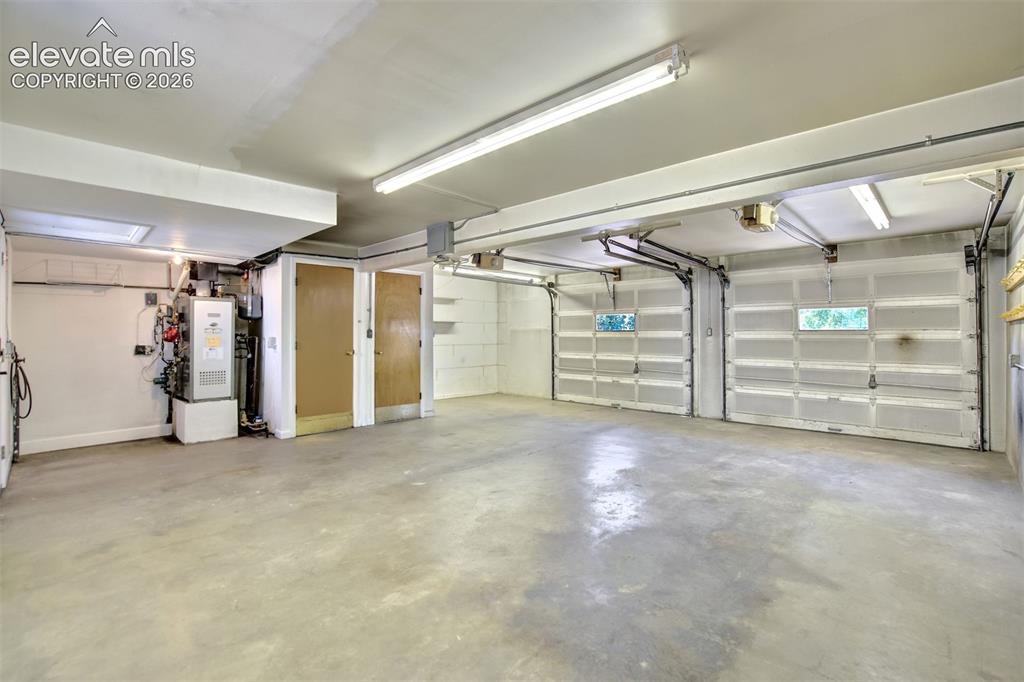 Image 44 of 50: Two-car garage featuring concrete flooring, fluorescent overhead lighting, 
