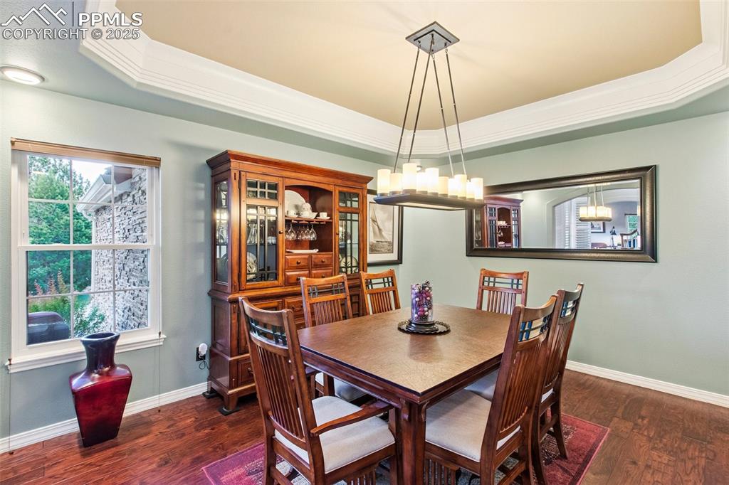Image 10 of 44: Dining area featuring a raised ceiling, dark wood-style flooring, a chandel