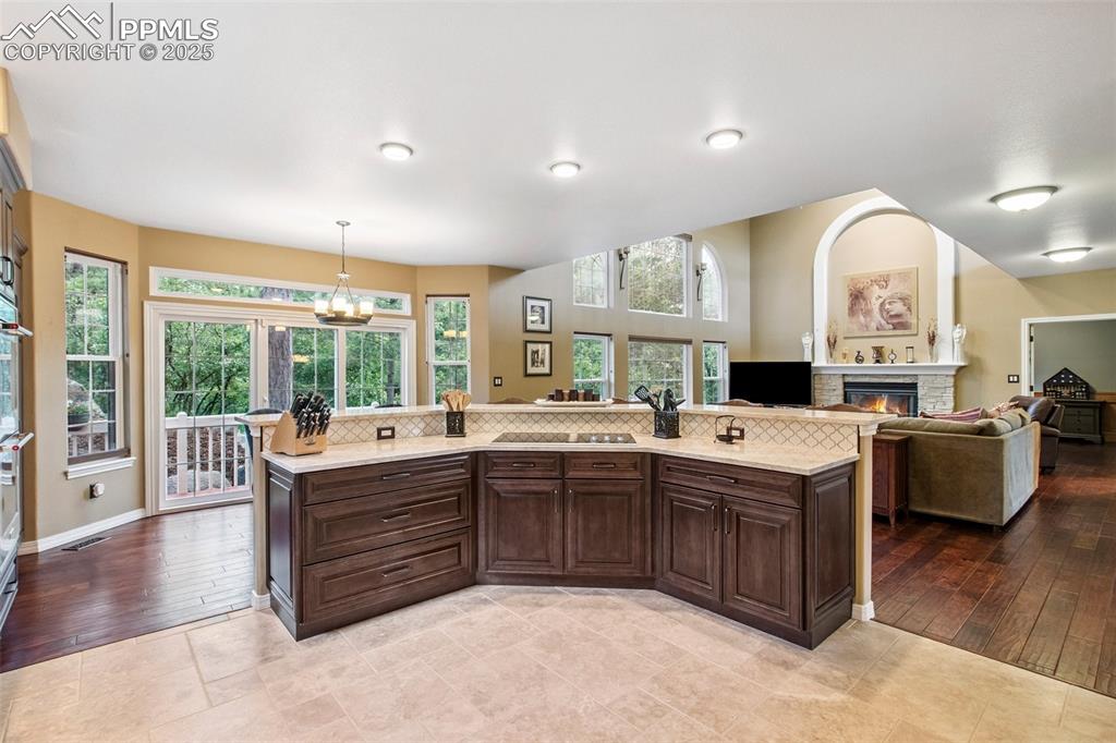 Image 13 of 44: Kitchen featuring light countertops, a glass covered fireplace, dark brown