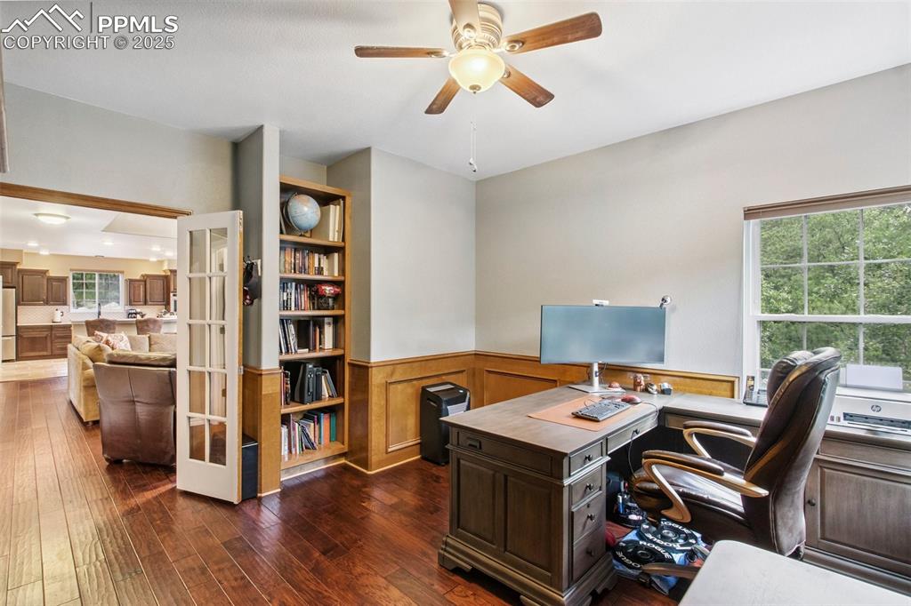 Image 14 of 44: Home office with a wainscoted wall, ceiling fan, dark wood-style flooring,
