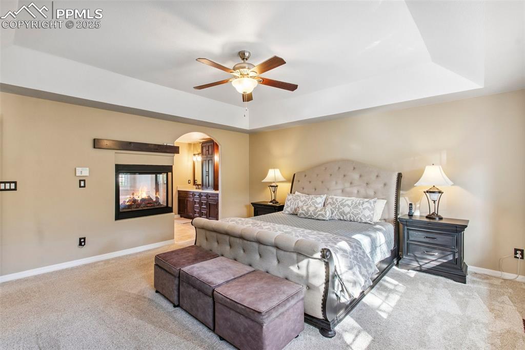 Image 21 of 44: Bedroom with a tray ceiling, carpet, arched walkways, ensuite bathroom, and