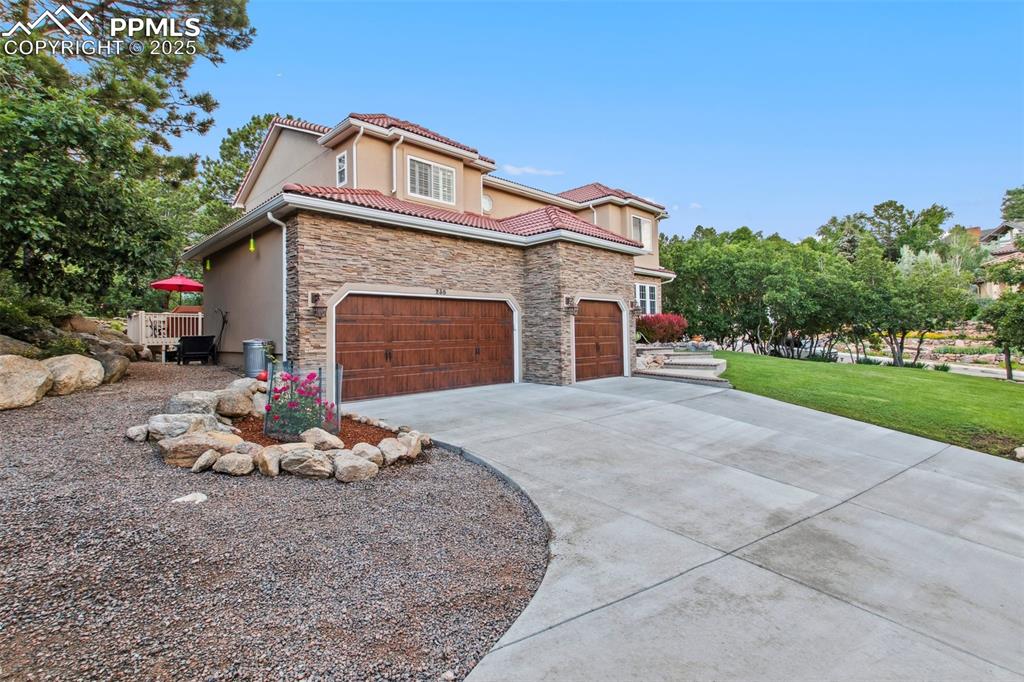 Image 4 of 44: View of side of property with concrete driveway, stone siding, a yard, a ti