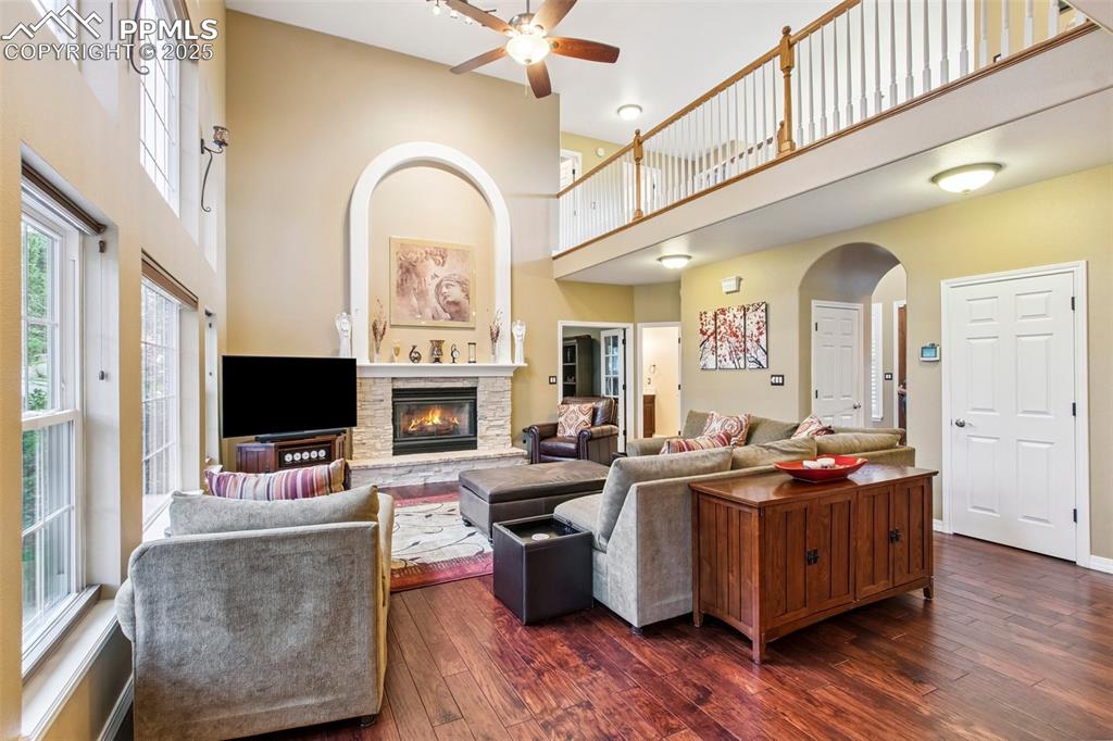 Image 9 of 44: Living area featuring a high ceiling, a ceiling fan, a fireplace, dark wood