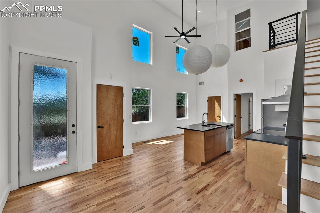 Image 25 of 49: Kitchen with light wood-style floors, ceiling fan, an island with sink, mod
