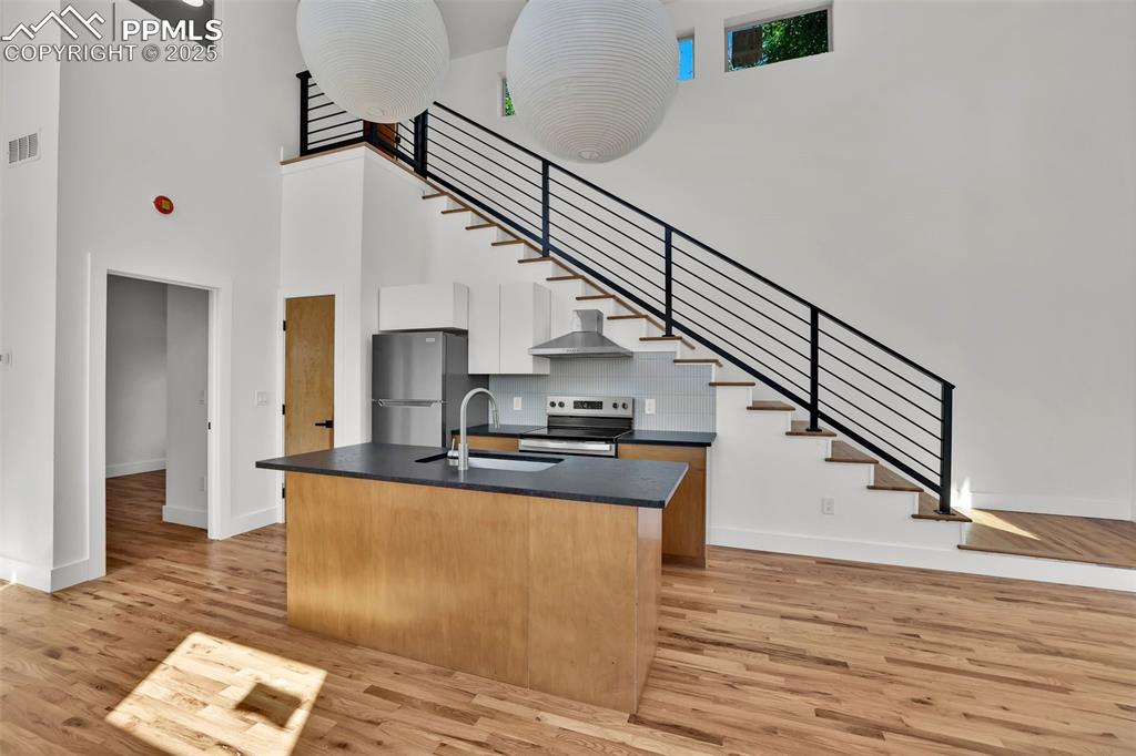 Image 28 of 49: Kitchen with dark countertops, a towering ceiling, light wood-style floors,