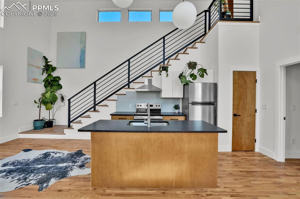 Image 9 of 49: Kitchen featuring dark countertops, a towering ceiling, light wood finished