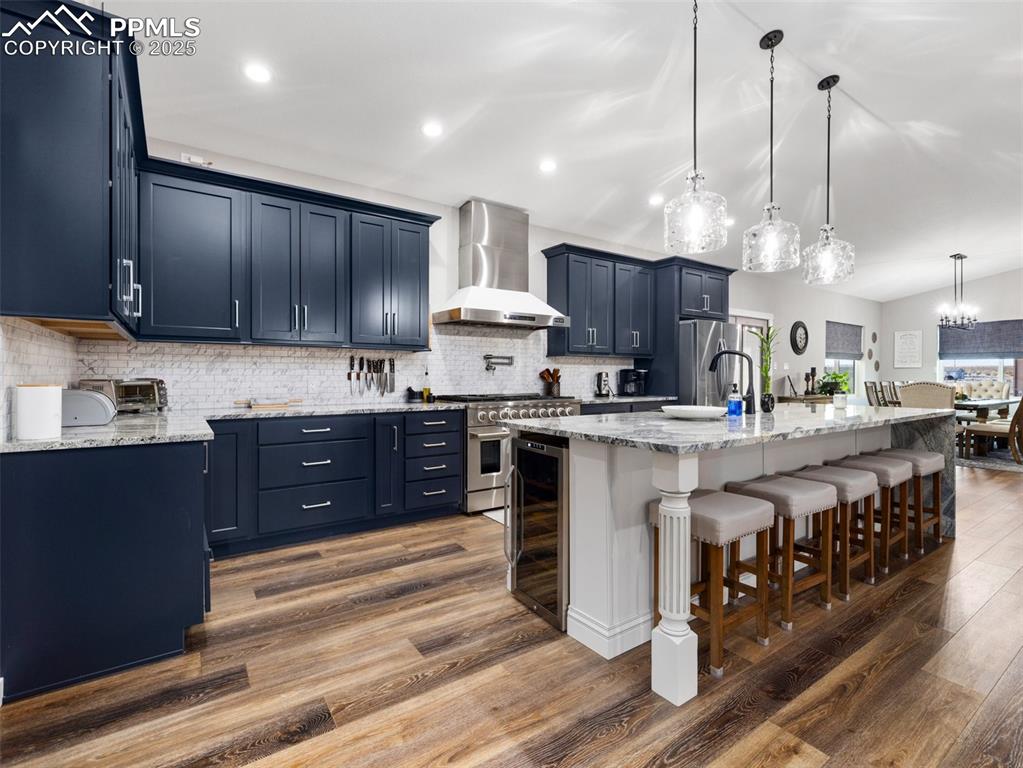 Image 18 of 48: Kitchen with wall chimney exhaust hood, stainless steel appliances, dark wo