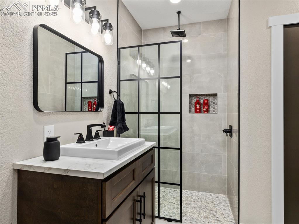 Image 47 of 48: Full bath with vanity, a textured wall, and a tile shower