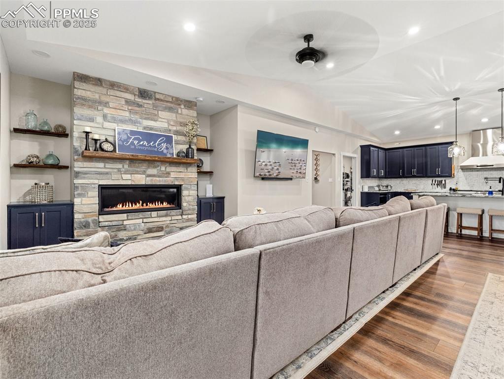 Image 5 of 48: Living room featuring dark wood-style floors, a stone fireplace, vaulted ce