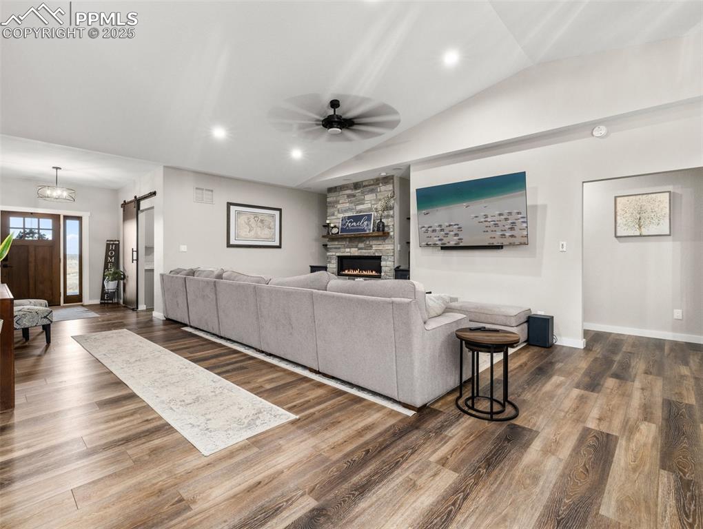 Image 6 of 48: Living area with a barn door, a fireplace, vaulted ceiling, ceiling fan, an