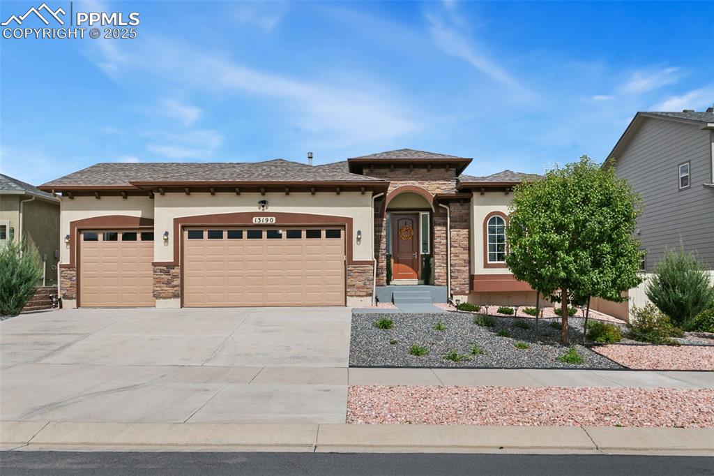 Caption: View of front of property featuring stucco siding, stone siding, an attached garage, and concrete dr