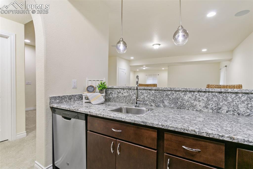 Image 27 of 49: Bar featuring dishwasher, brown cabinetry, light stone countertops, pendant