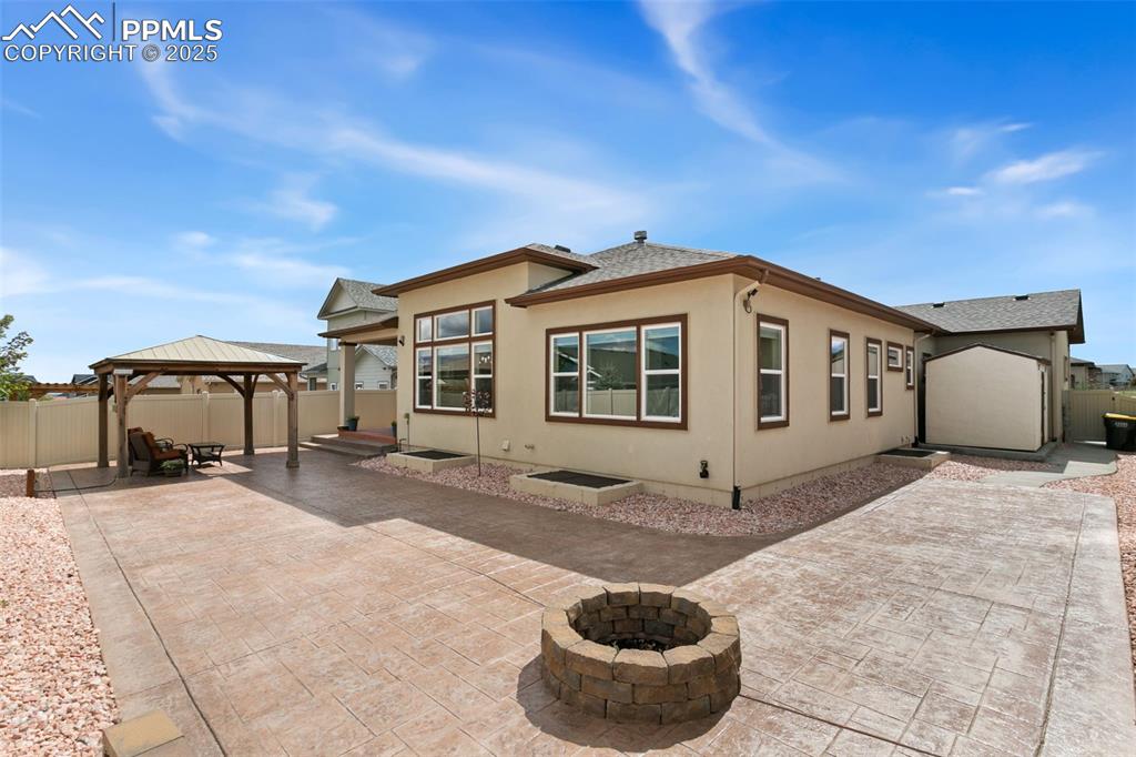 Image 38 of 49: Back of house featuring a fire pit, a gazebo, a patio area, roof with shing