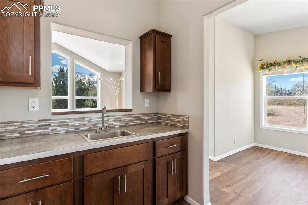 Image 10 of 50: Kitchen with baseboards, wood finished floors, a sink, and tasteful backspl