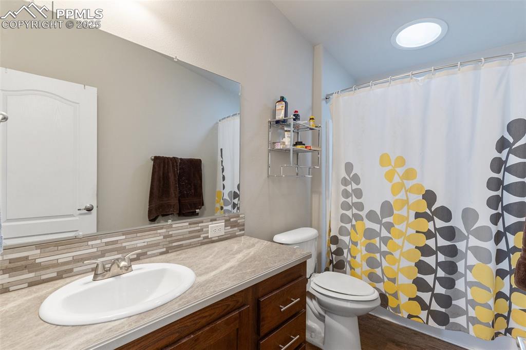 Image 22 of 50: Bathroom featuring curtained shower, toilet, vanity, and decorative backspl
