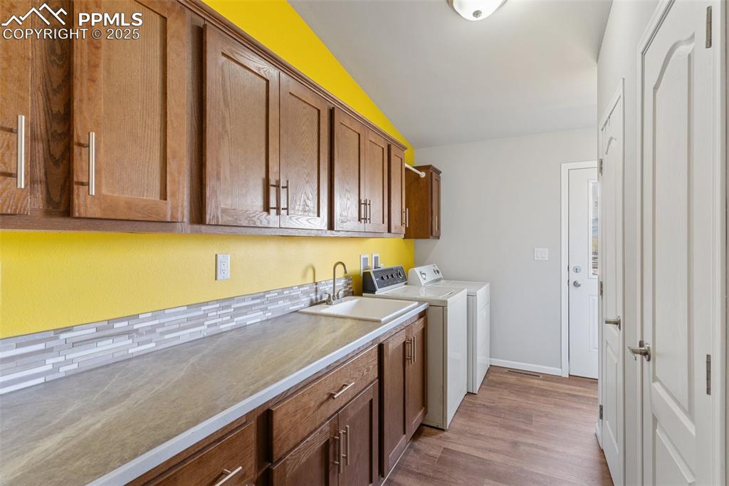 Image 23 of 50: Laundry room with a sink, baseboards, wood finished floors, cabinet space, 