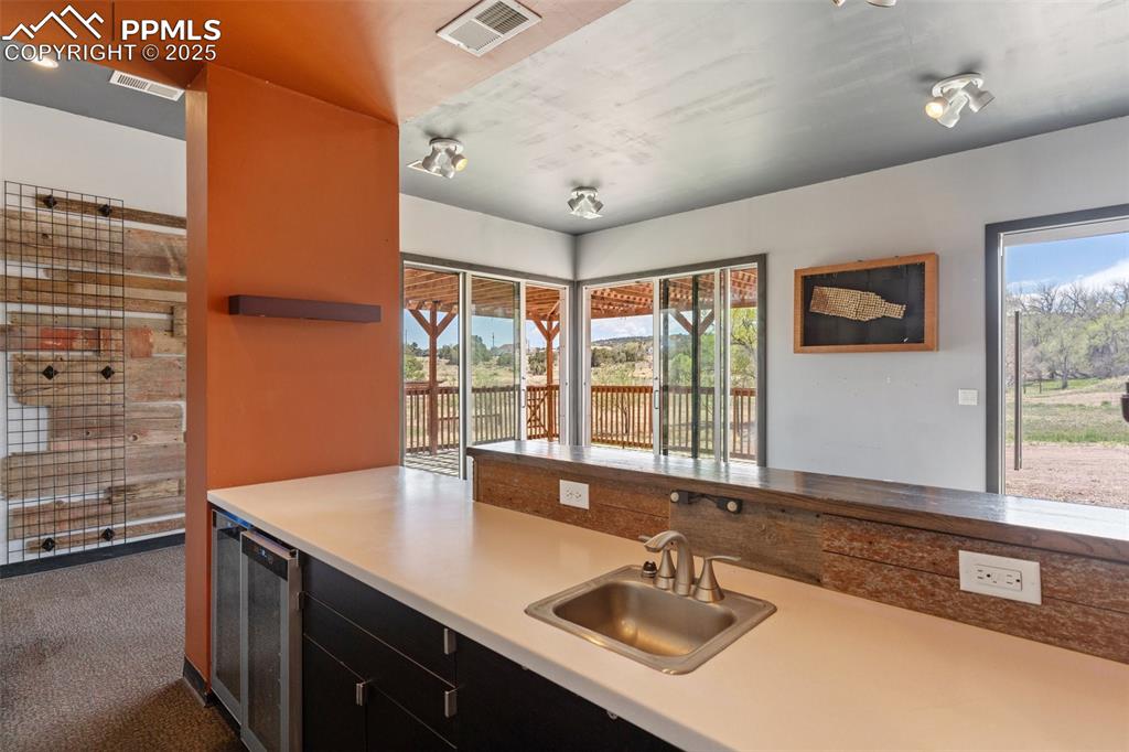 Image 40 of 50: Kitchen featuring dark colored carpet, beverage cooler, a sink, and visible