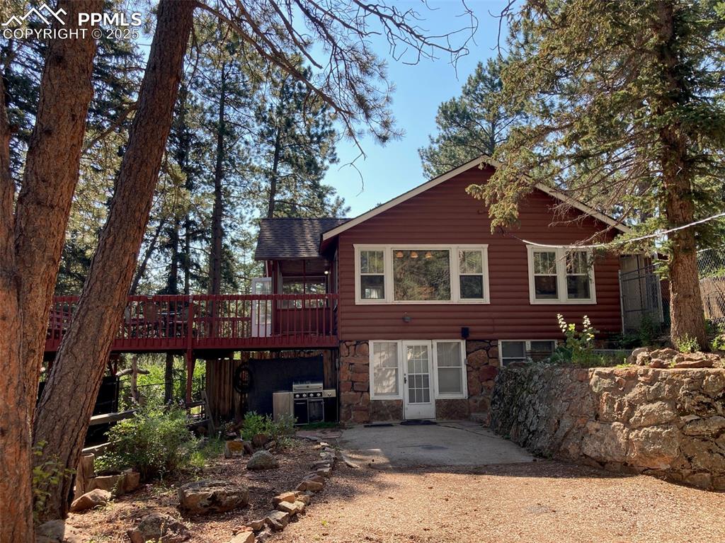 Caption: Back of property with stone siding, a wooden deck, faux log siding, and a patio
