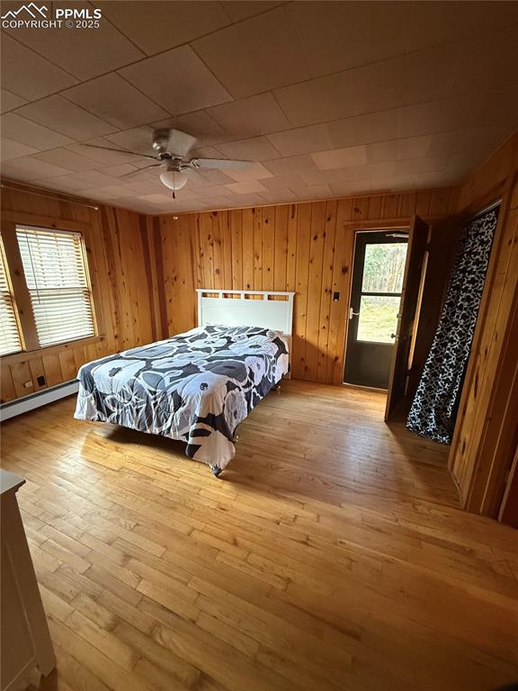 Image 10 of 23: Bedroom with light wood finished floors, a baseboard heating unit, wood wal