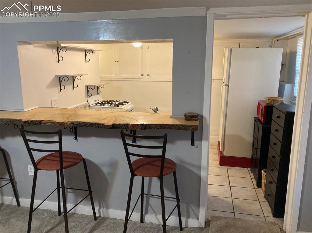 Image 19 of 23: Kitchen with freestanding refrigerator, a breakfast bar area, light tile pa