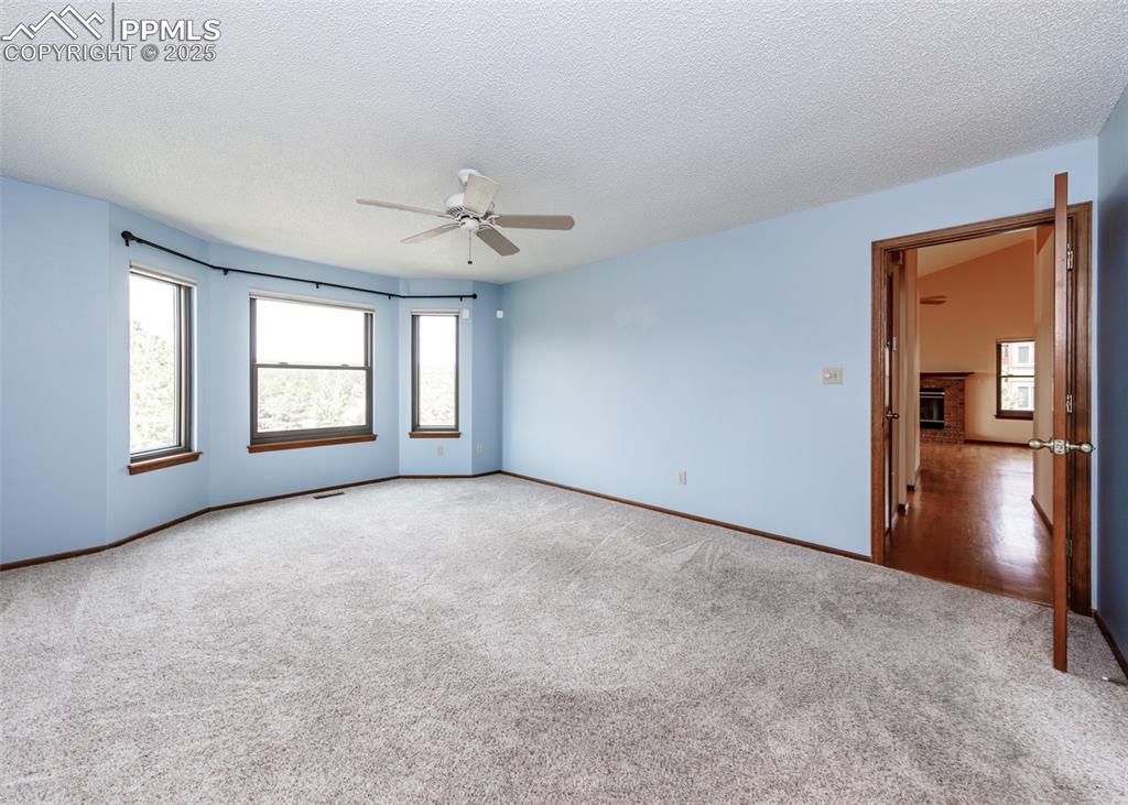 Image 19 of 44: Unfurnished room featuring a textured ceiling, ceiling fan, a fireplace, an