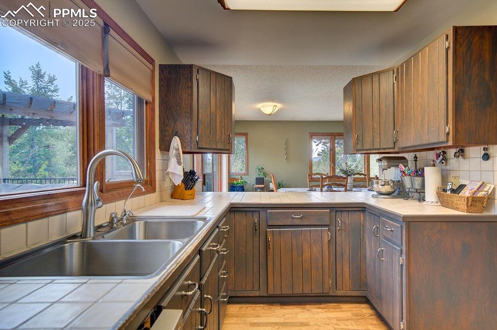 Image 12 of 42: Kitchen featuring a peninsula, tile counters, tasteful backsplash, a sink,
