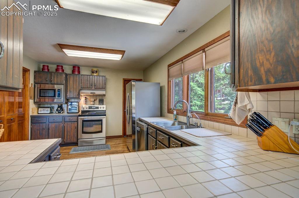 Image 15 of 42: Kitchen featuring tile counters, under cabinet range hood, tasteful backspl