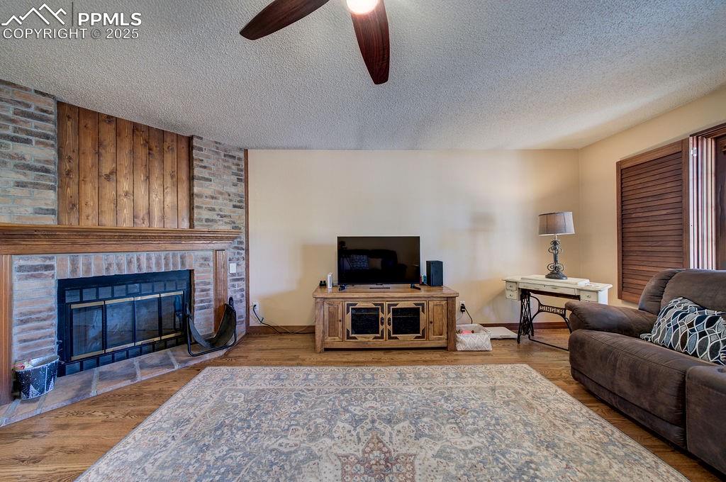 Image 26 of 42: Living area with a fireplace, a ceiling fan, a textured ceiling, and wood f