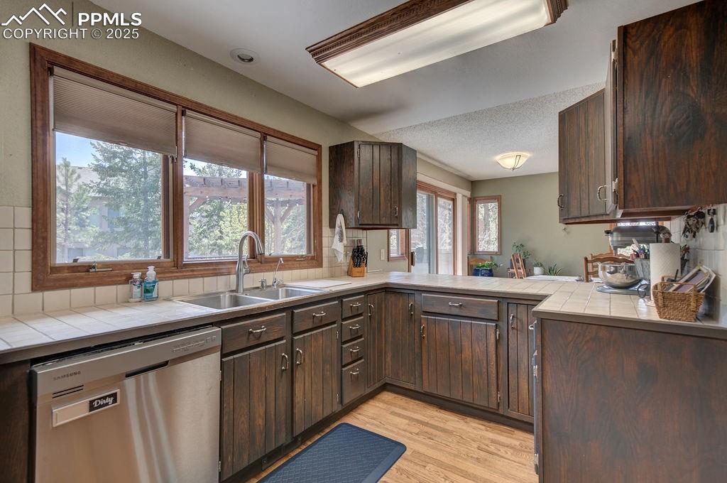 Image 30 of 42: Kitchen with a sink, tile counters, stainless steel dishwasher, and dark br