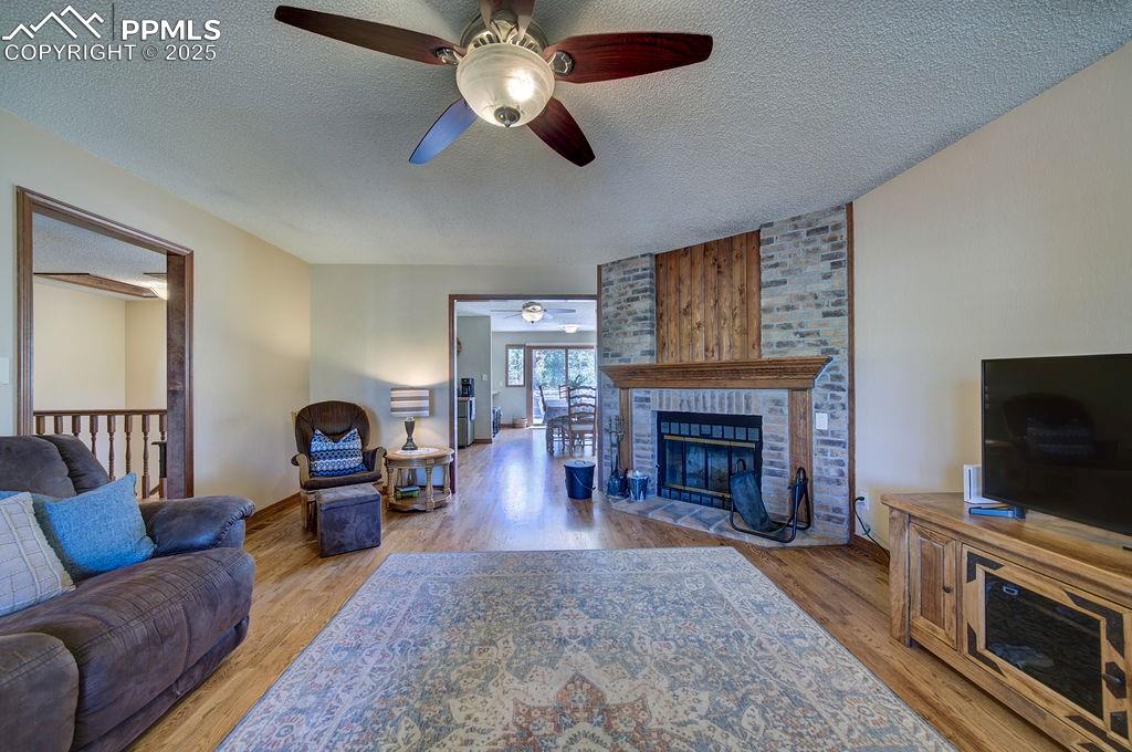 Image 4 of 42: Living area featuring a brick fireplace, a ceiling fan, a textured ceiling,