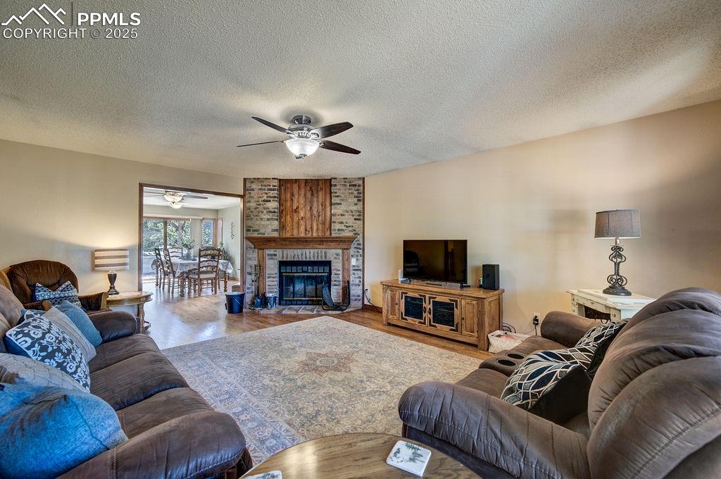 Image 5 of 42: Living area with a brick fireplace, a textured ceiling, ceiling fan, and wo