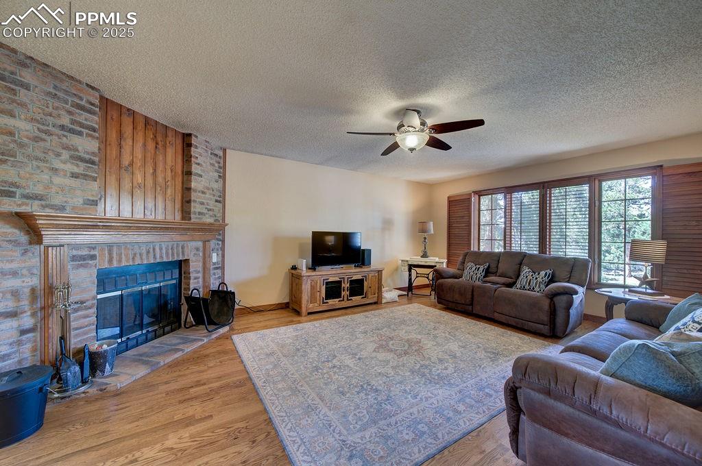 Image 7 of 42: Living room with a ceiling fan, a textured ceiling, a brick fireplace, and