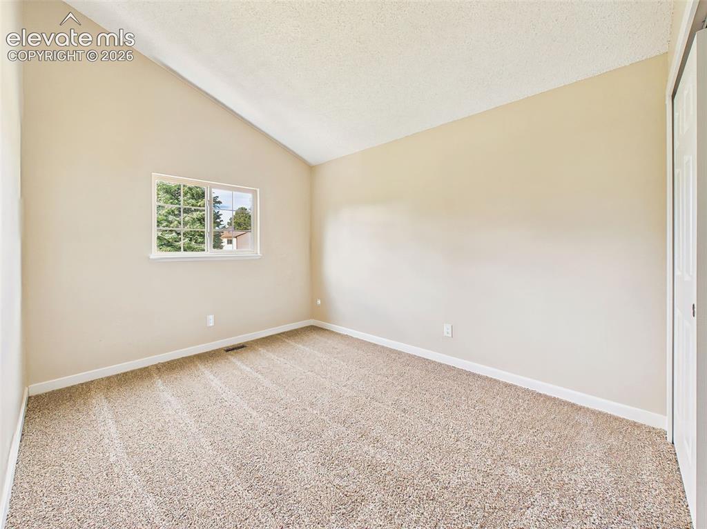 Image 32 of 50: Secondary bedroom with vaulted ceilings, new carpet, neutral finishes, and