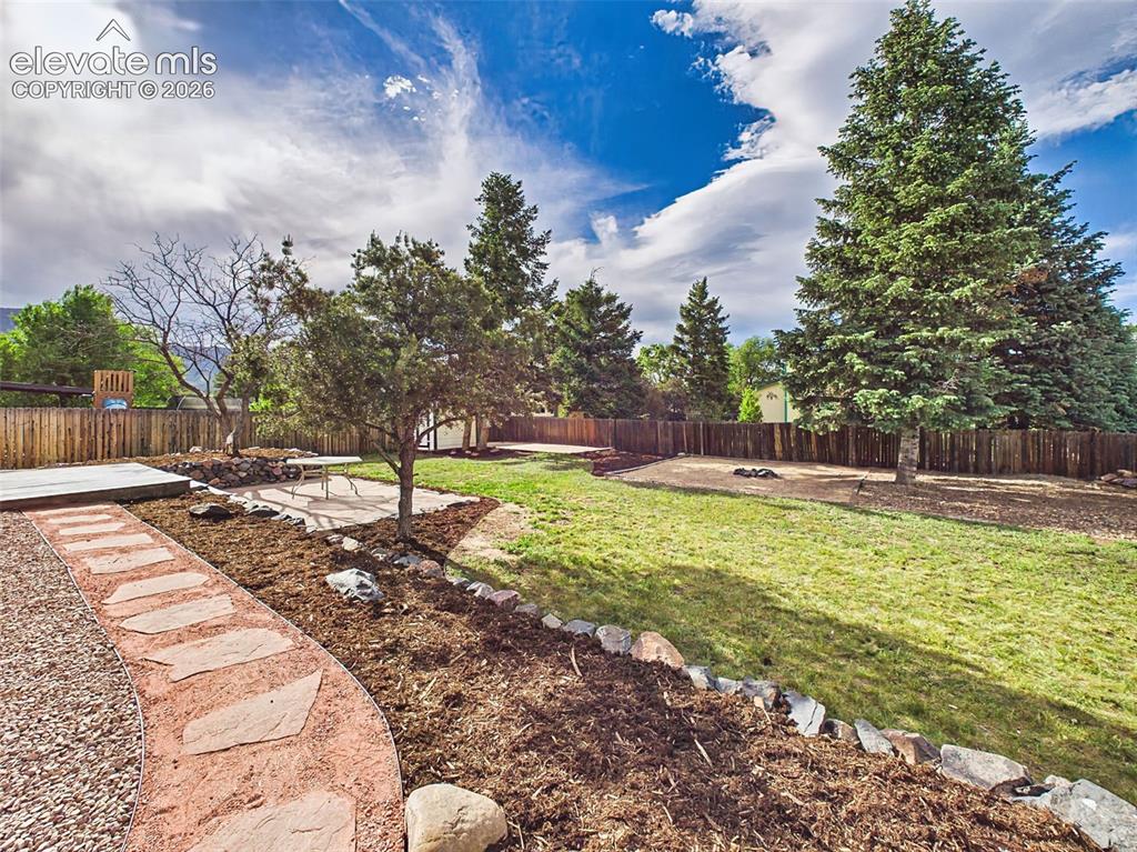 Image 41 of 50: Expansive fenced backyard with mature trees, established landscaping, flags