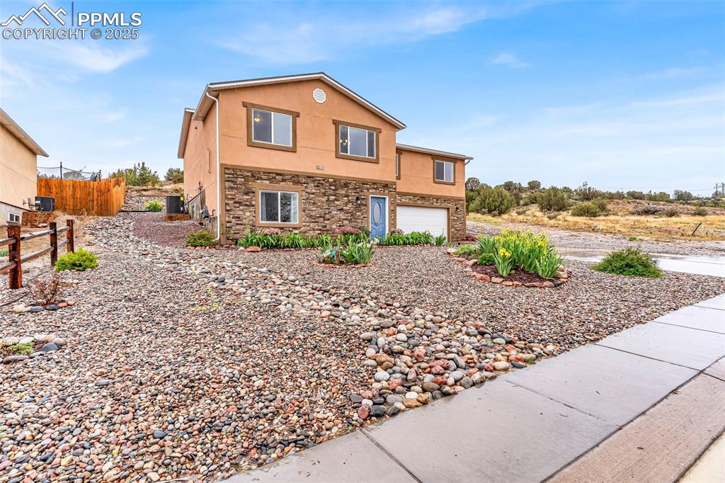 Image 2 of 50: View of side of property with stucco siding, stone siding, an attached gara
