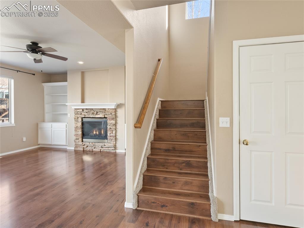 Image 19 of 46: Stairs featuring a ceiling fan, wood finished floors, a stone fireplace, an