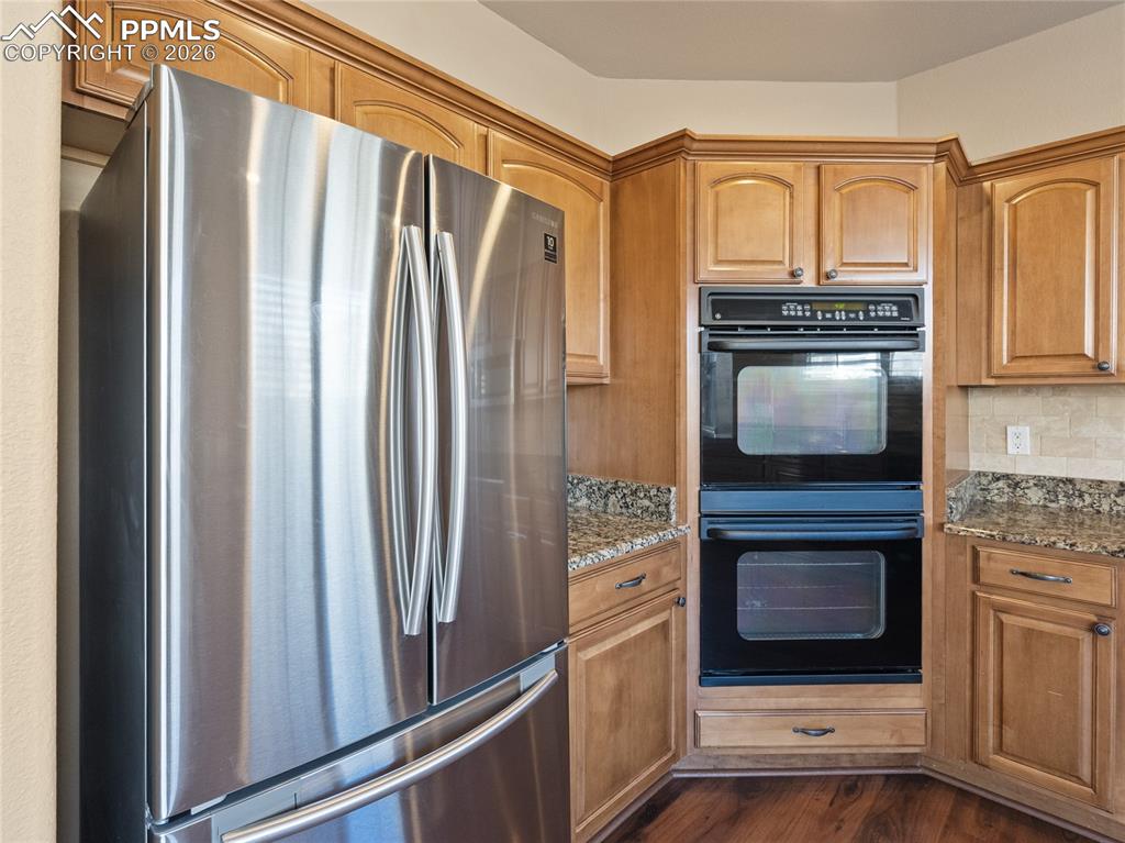 Image 8 of 46: Kitchen with freestanding refrigerator, light stone countertops, dark wood