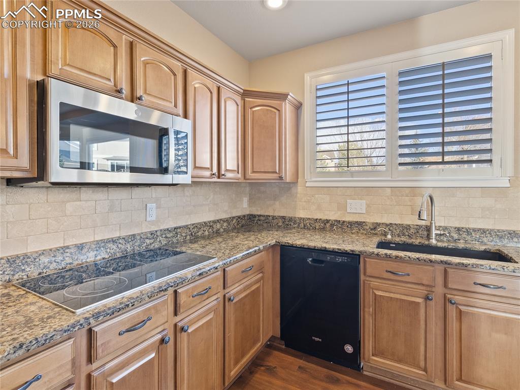 Image 9 of 46: Kitchen featuring appliances, dark stone counters, and tasteful backsplash