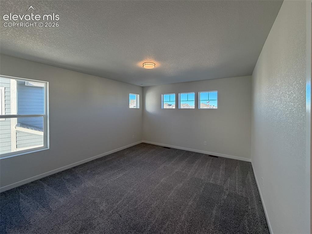 Image 20 of 34: Recessed lighting, multiple windows, textured walls, and dark gray carpetin
