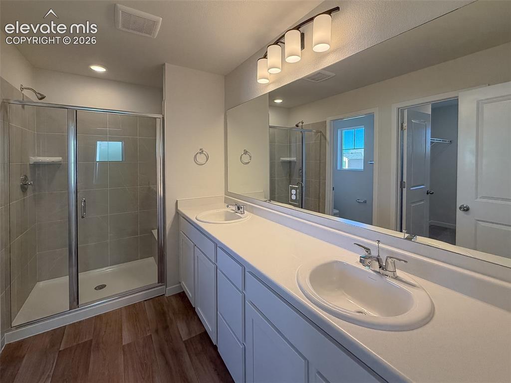 Image 21 of 34: Double vanity with integrated sinks, wood-finish flooring, glass-enclosed s