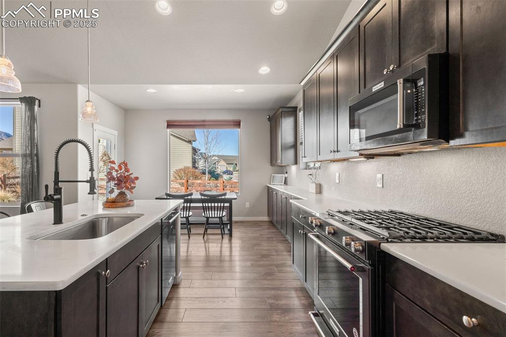 Image 12 of 48: Kitchen featuring stainless steel appliances, dark brown cabinetry, pendant