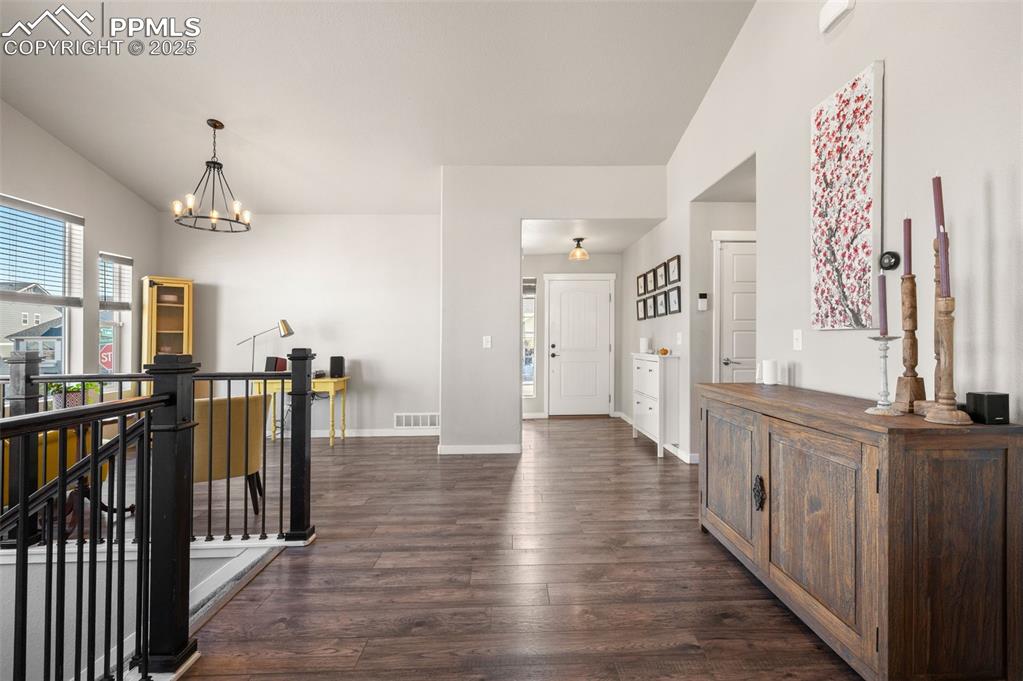 Image 14 of 48: Foyer entrance with dark wood-style flooring, a chandelier, and vaulted cei