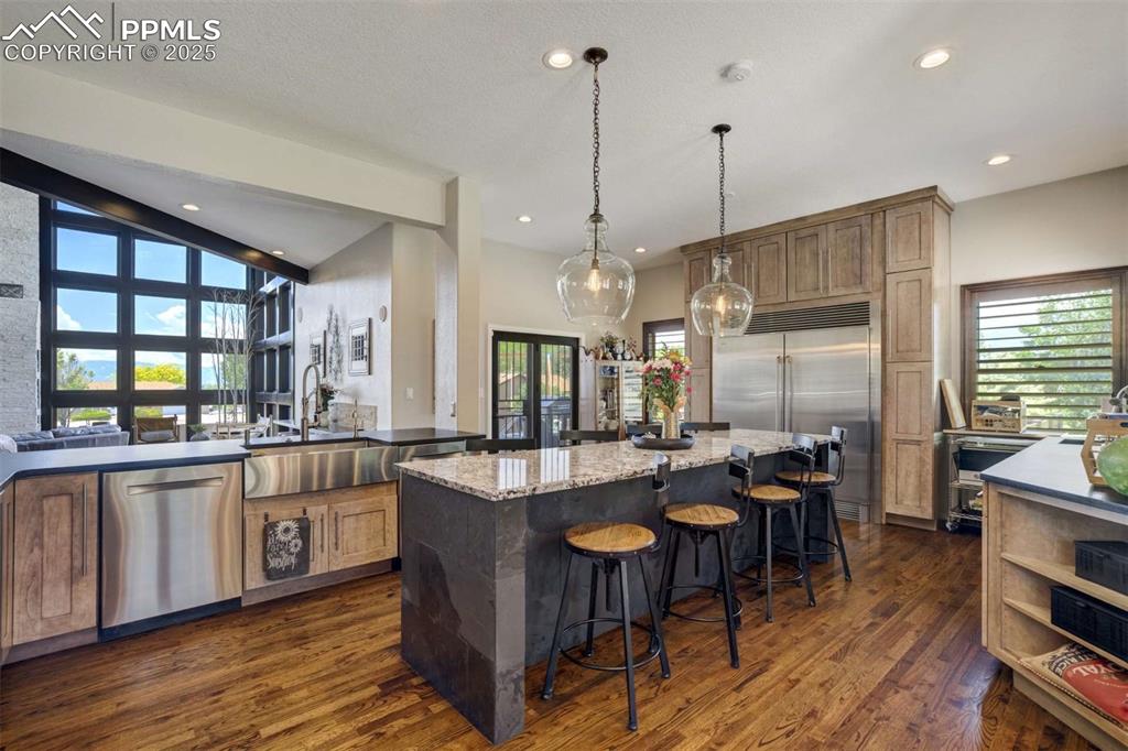Image 13 of 50: Kitchen with dark stone counters, stainless steel appliances, dark wood-sty