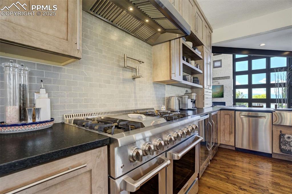 Image 15 of 50: Kitchen with stainless steel appliances, custom range hood, backsplash, dar